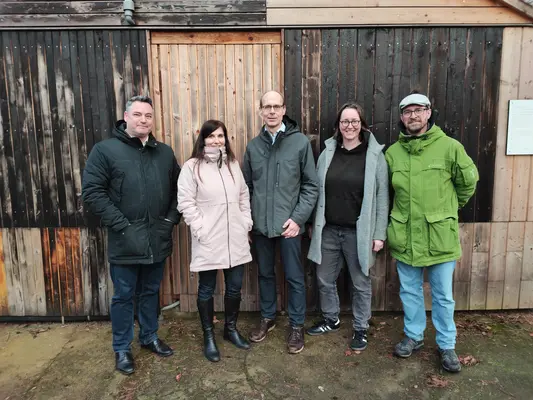 Projektstart 5 Personen stehen im Halbkreis vor einer Holzwand